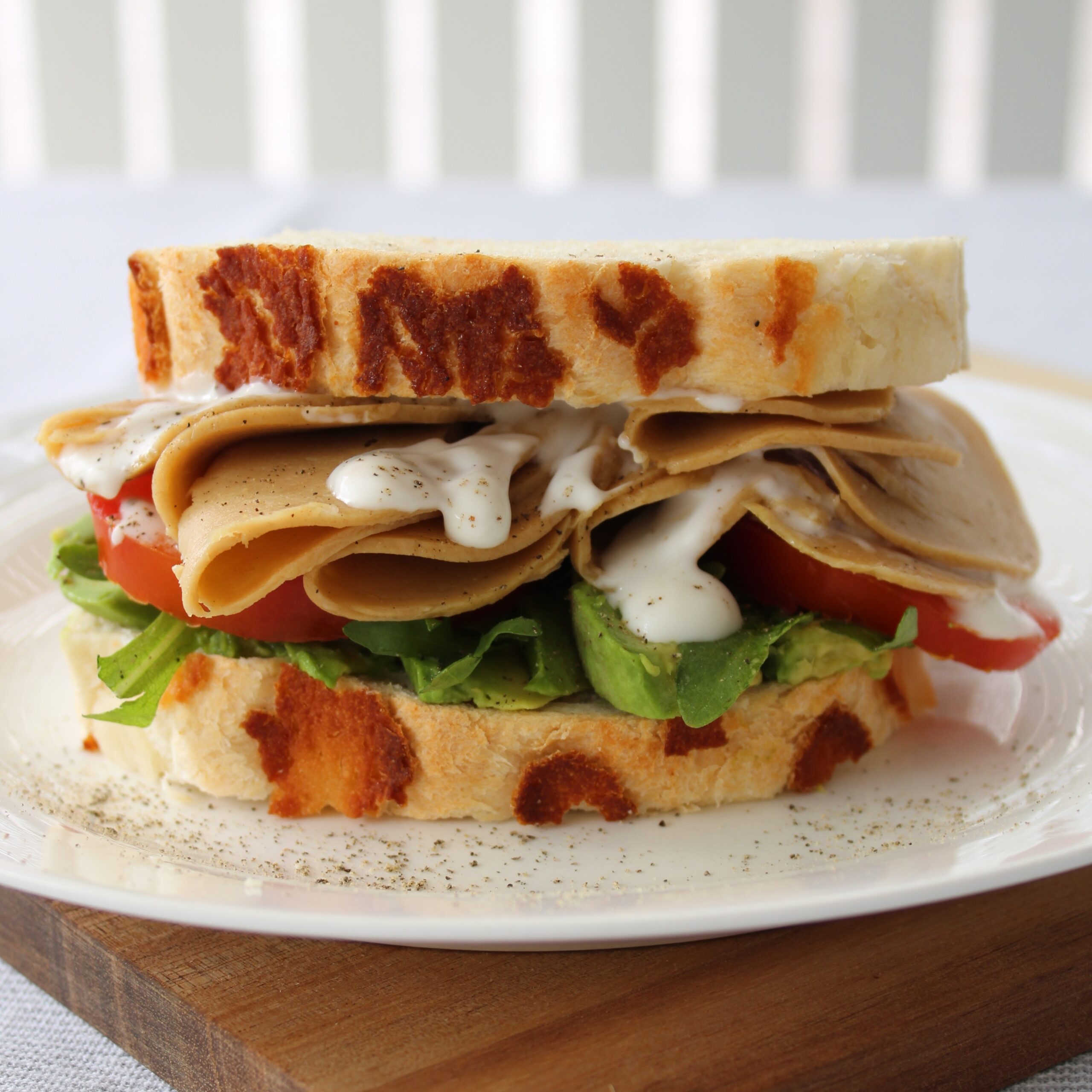 A sandwich made with white bread, salad and Made With Plants vegan chicken sits on a white plate